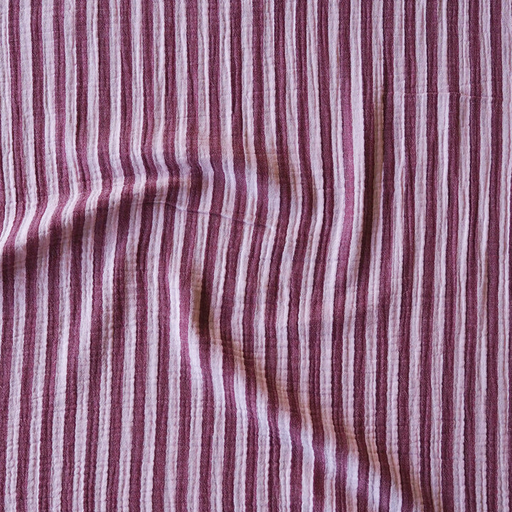 A close-up of a striped fabric with vertical stripes in dusty rose, mauve, and white, showing a textured woven material with soft folds.