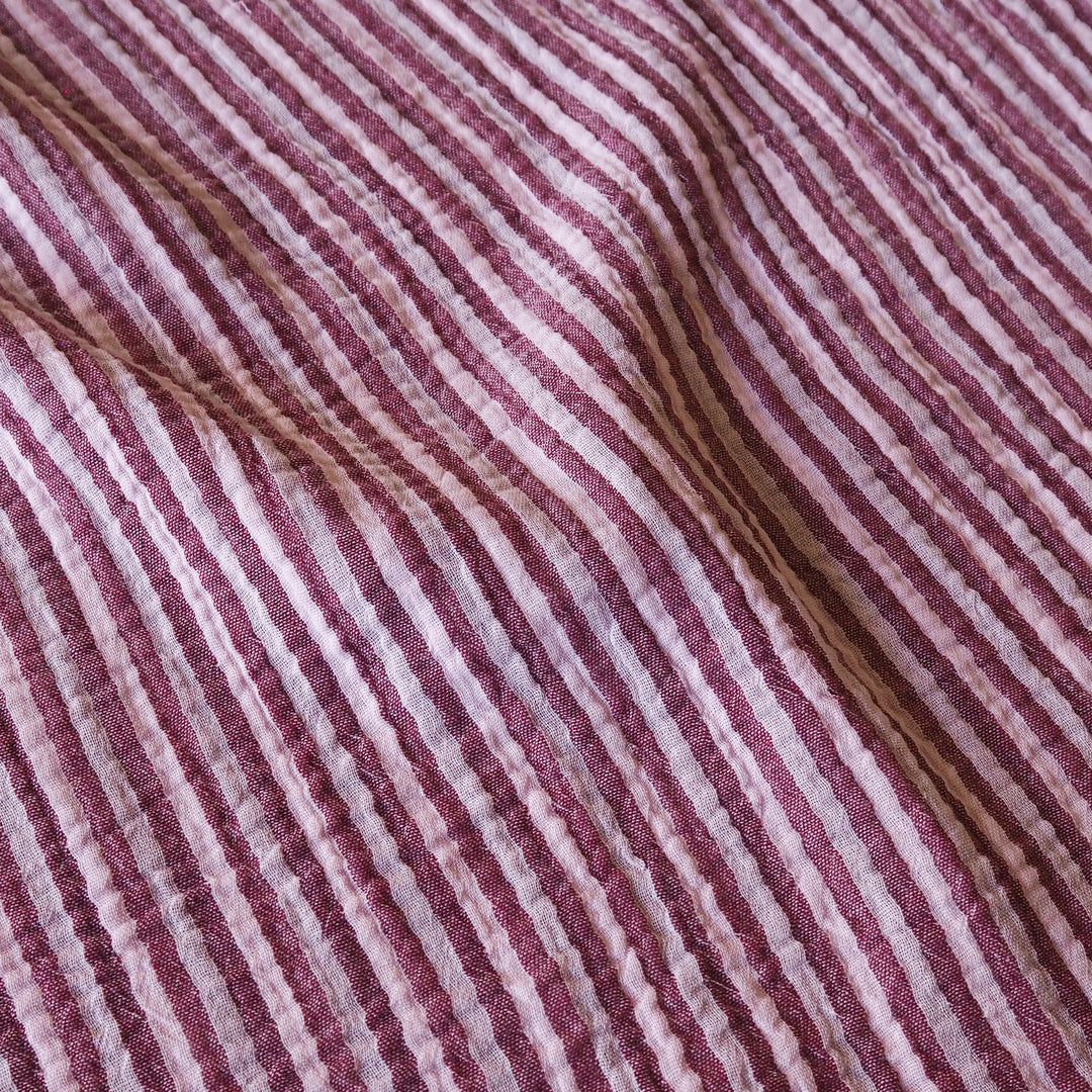A close-up of a textured fabric with vertical stripes in dusty rose, mauve, and white, with a few thin brown threads running through it.