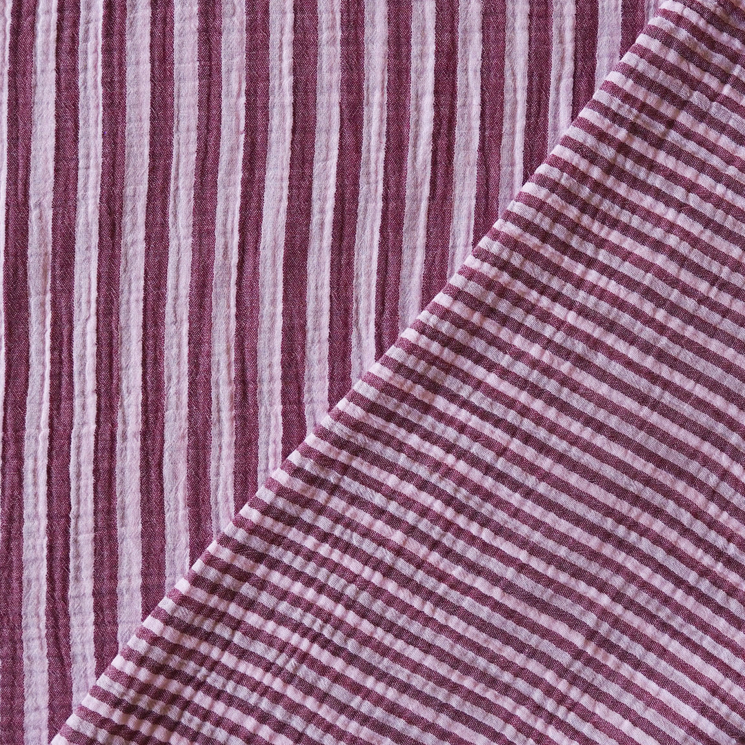 A close-up of a woven textile with alternating vertical stripes in dusty burgundy and off-white, folded diagonally to show texture and pattern.