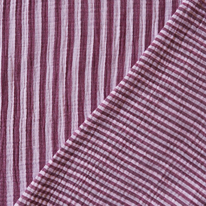 A close-up of a woven textile with alternating vertical stripes in dusty burgundy and off-white, folded diagonally to show texture and pattern.