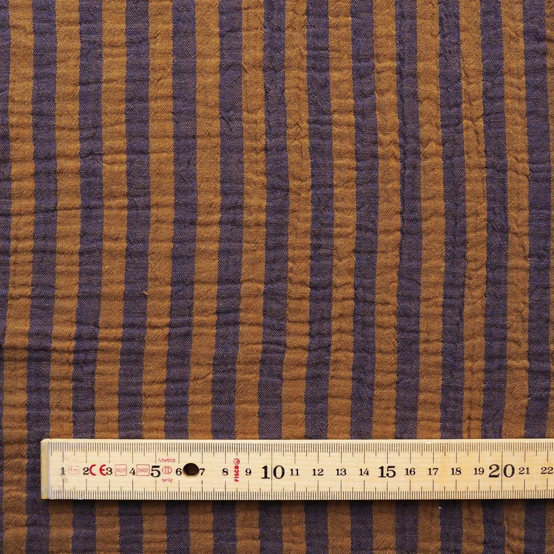 A close-up of a striped fabric with alternating brown and dark purple vertical bands, shown with a wooden ruler at the bottom for scale.