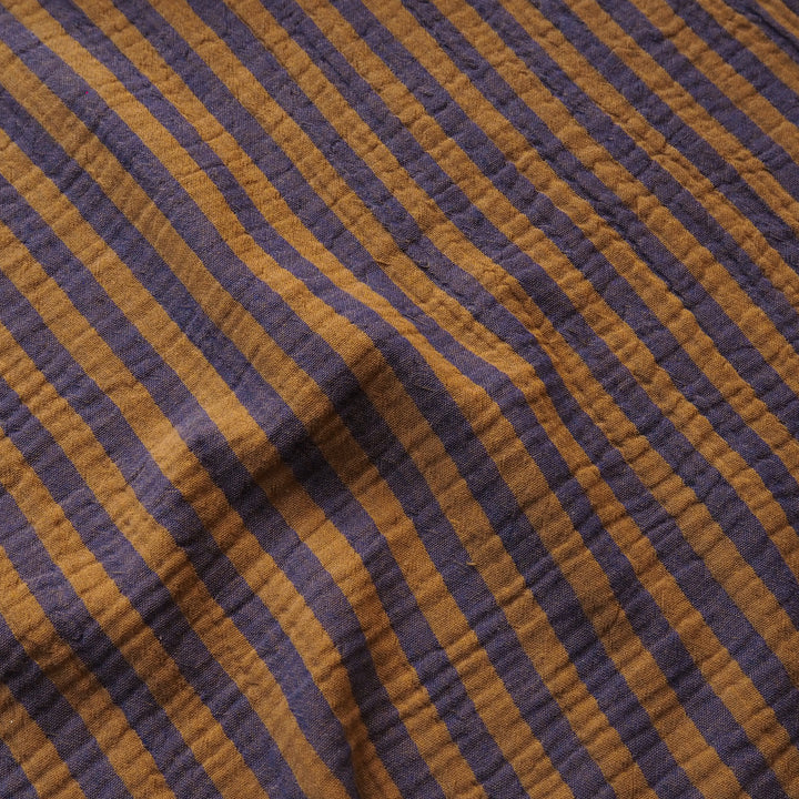 A close-up of a textured fabric with diagonal stripes in dark purple and warm mustard brown.