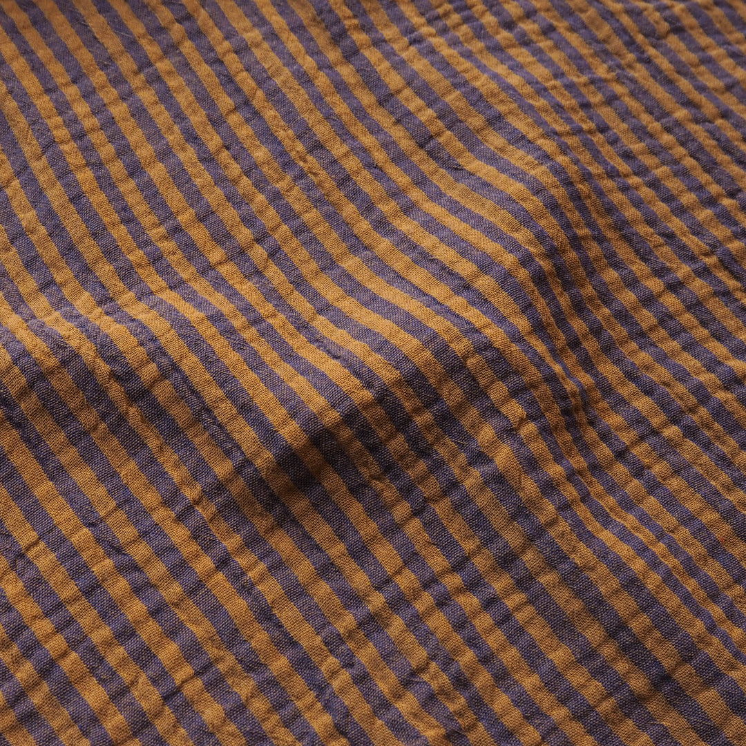 A close-up of a textured fabric with a diagonal striped pattern in mustard yellow and dark purple.