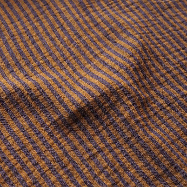 A close-up of a textured fabric with a diagonal striped pattern in mustard yellow and dark purple.