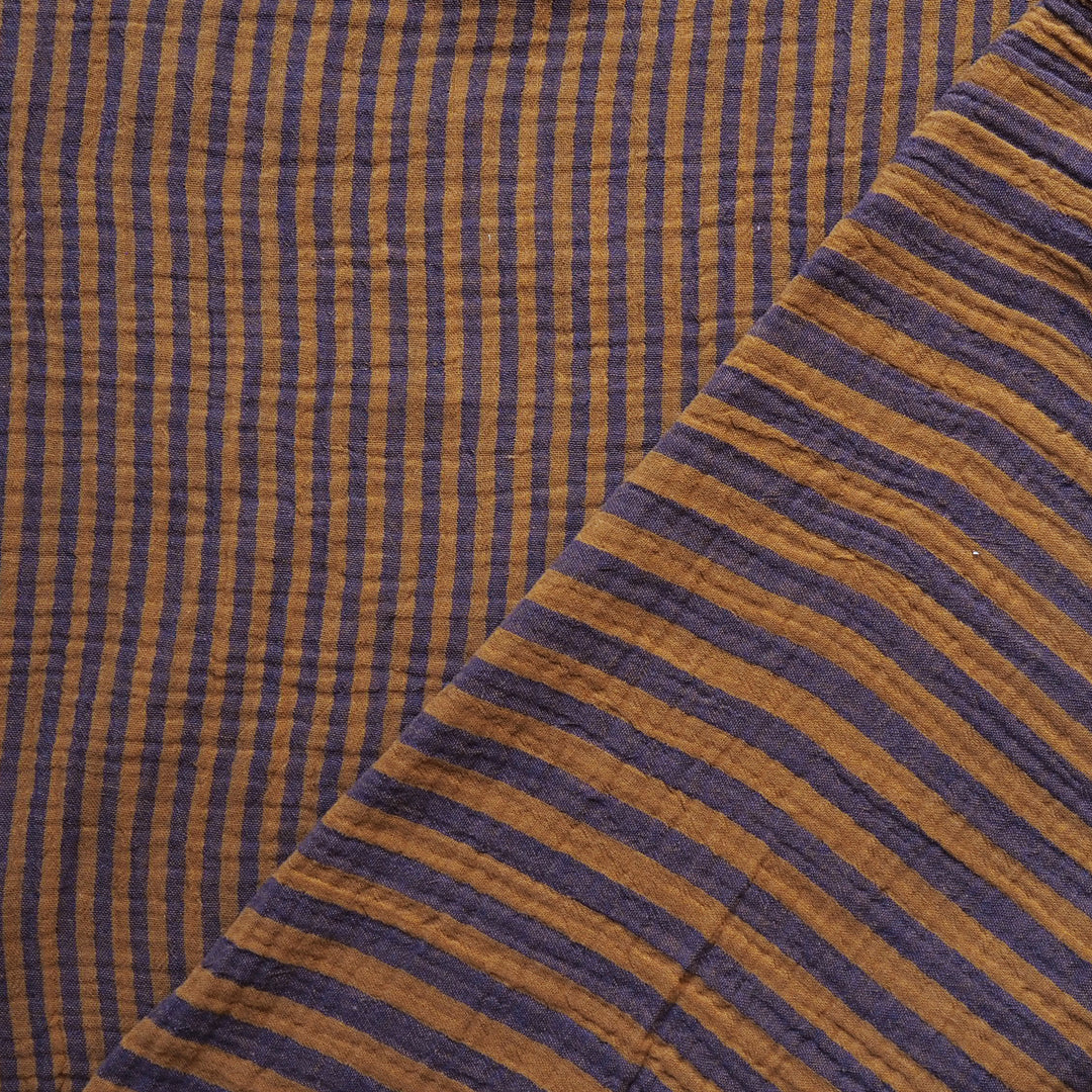 Close-up of a striped fabric with alternating vertical and diagonal bands in dark purple and warm mustard yellow, showing a textured, gauze-like weave.