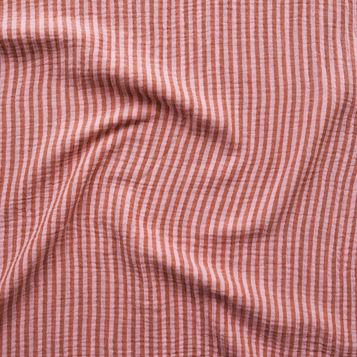 A close-up of a textured fabric with a fine vertical stripe pattern in dusty pink and muted red.