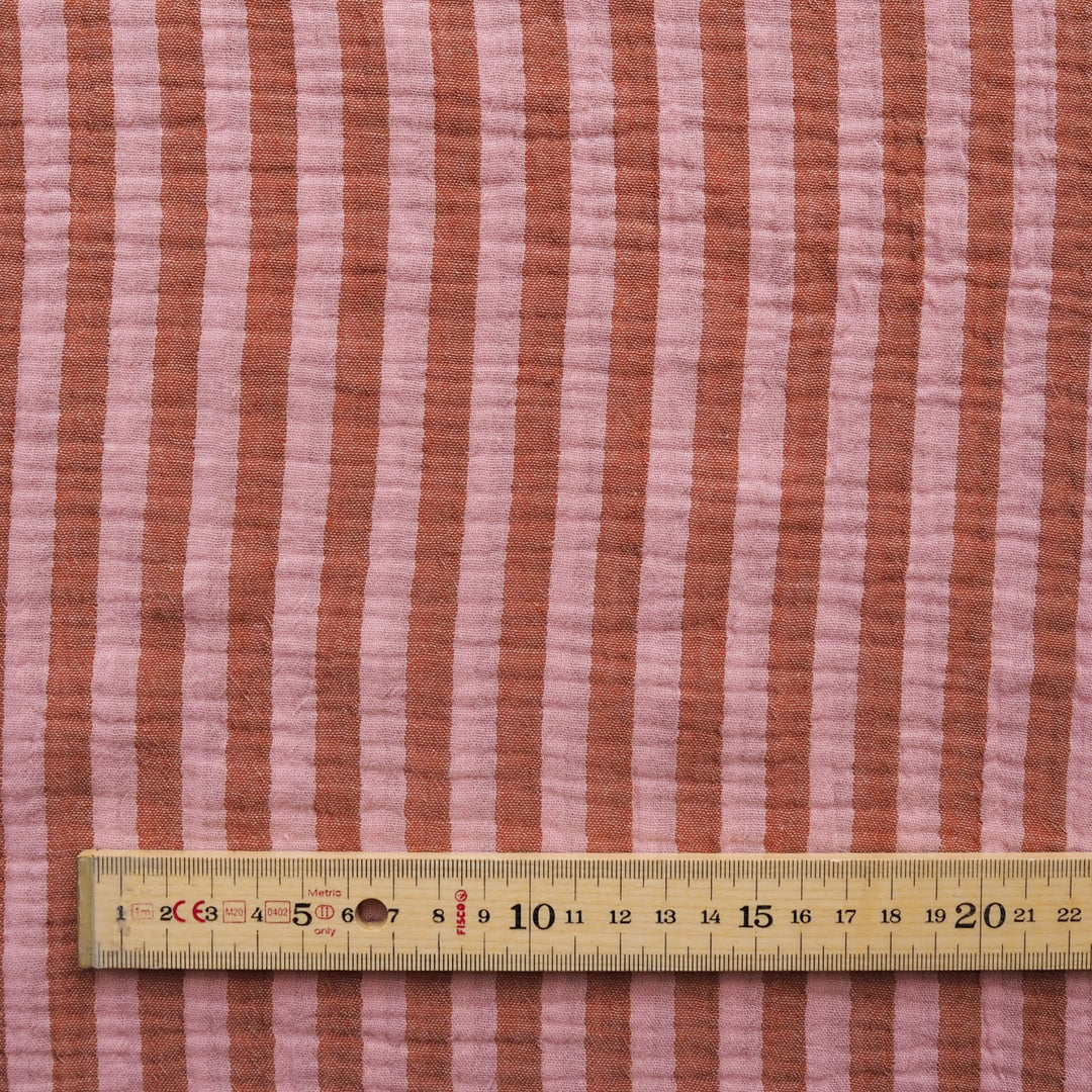 Pink and terracotta striped quilted fabric with a wooden ruler at the bottom for scale.