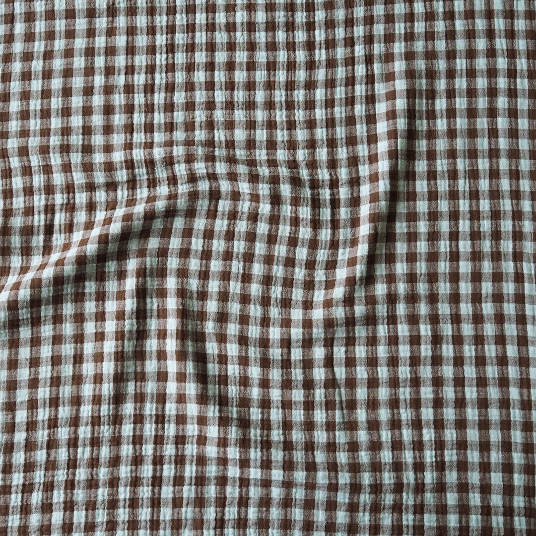 Brown and off-white checkered fabric with a crinkled gauze texture, shown with soft folds.