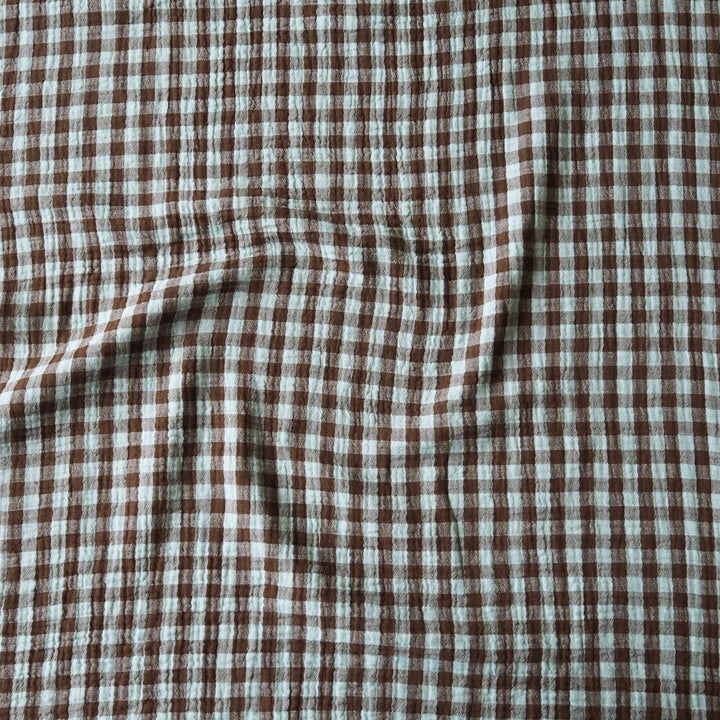 Brown and off-white checkered fabric with a crinkled gauze texture, shown with soft folds.