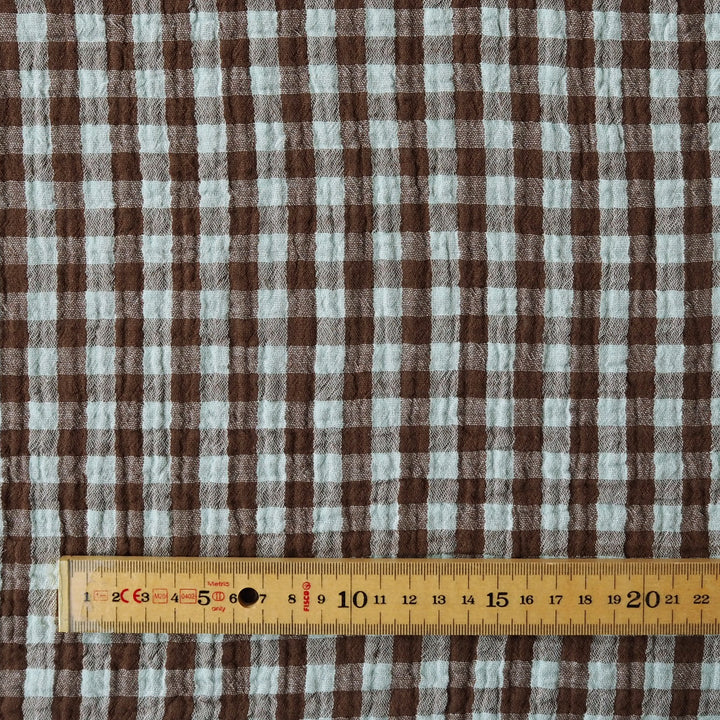 Brown and white gingham fabric pattern shown close up with a wooden ruler at the bottom for scale.