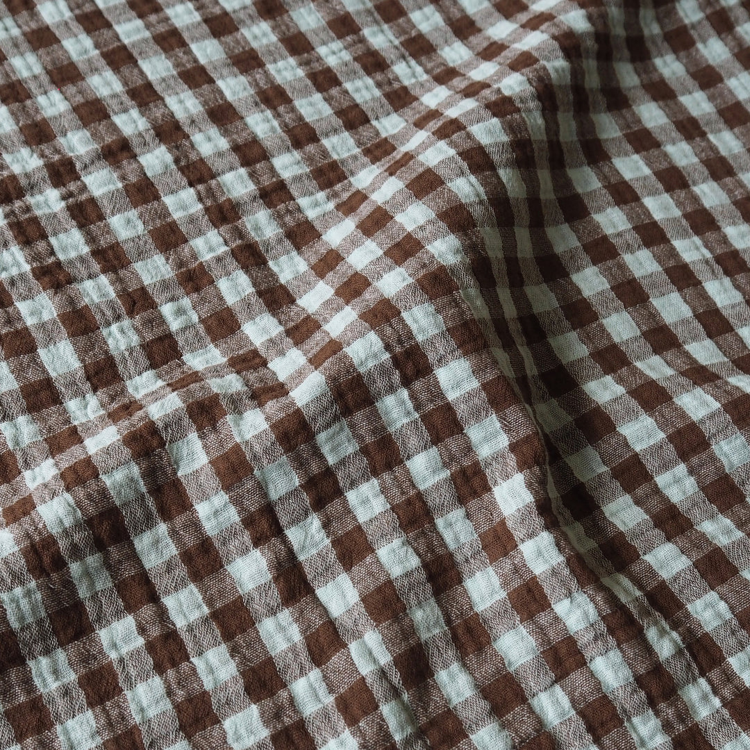 Brown and off-white gingham checkered fabric with a soft, textured weave, shown in a draped arrangement.