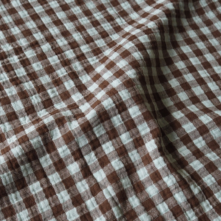 Brown and off-white gingham checkered fabric with a soft, textured weave, shown in a draped arrangement.