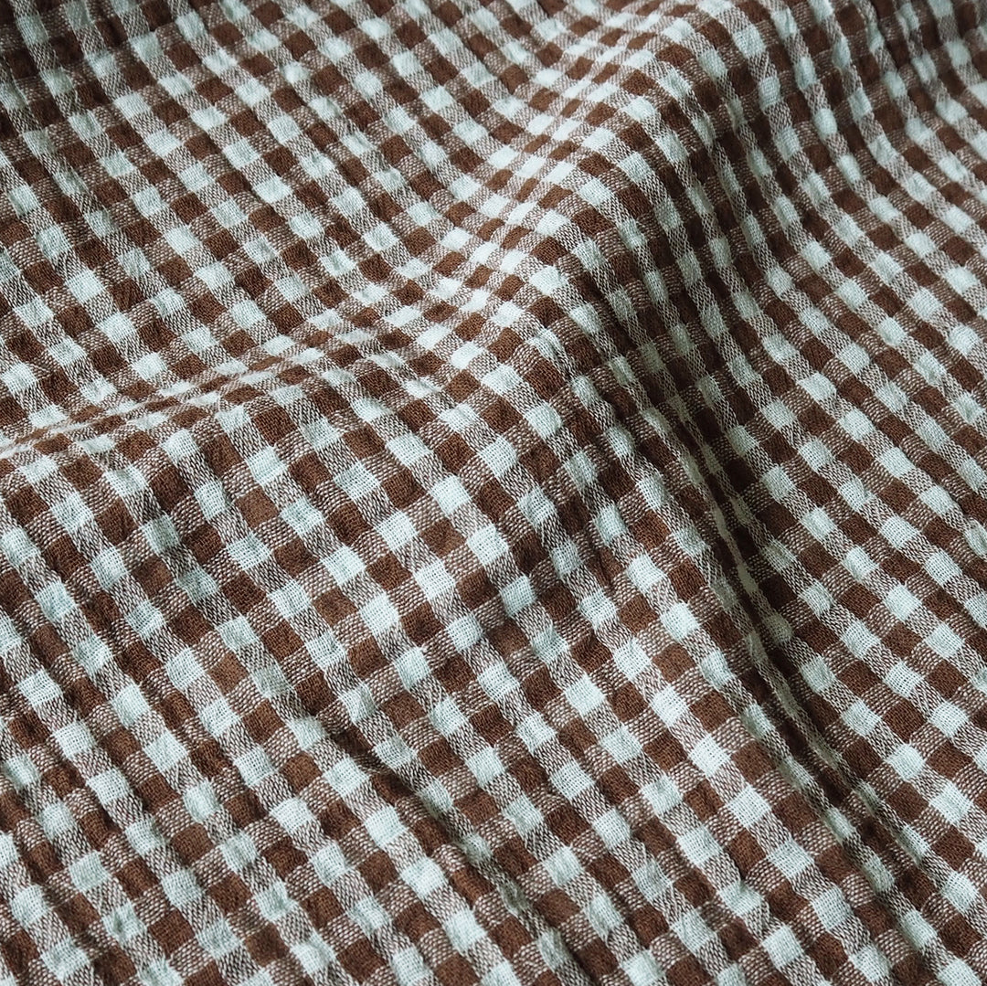 Brown and white gingham checkered fabric with a soft, textured weave, shown in gentle folds.
