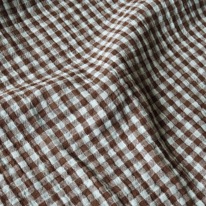Brown and white gingham checkered fabric with a soft, textured weave, shown in gentle folds.