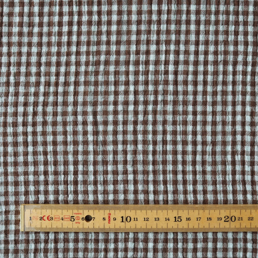 Brown and white gingham fabric pattern shown close up with a wooden ruler at the bottom for scale.