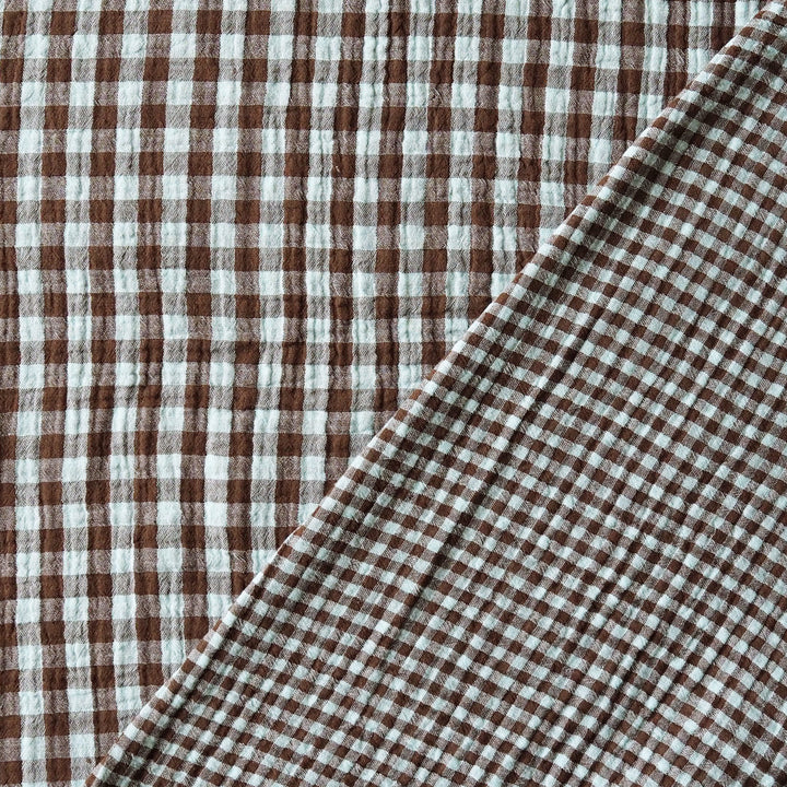 Brown and white gingham checkered fabric with a soft crinkled texture, folded diagonally across the frame.