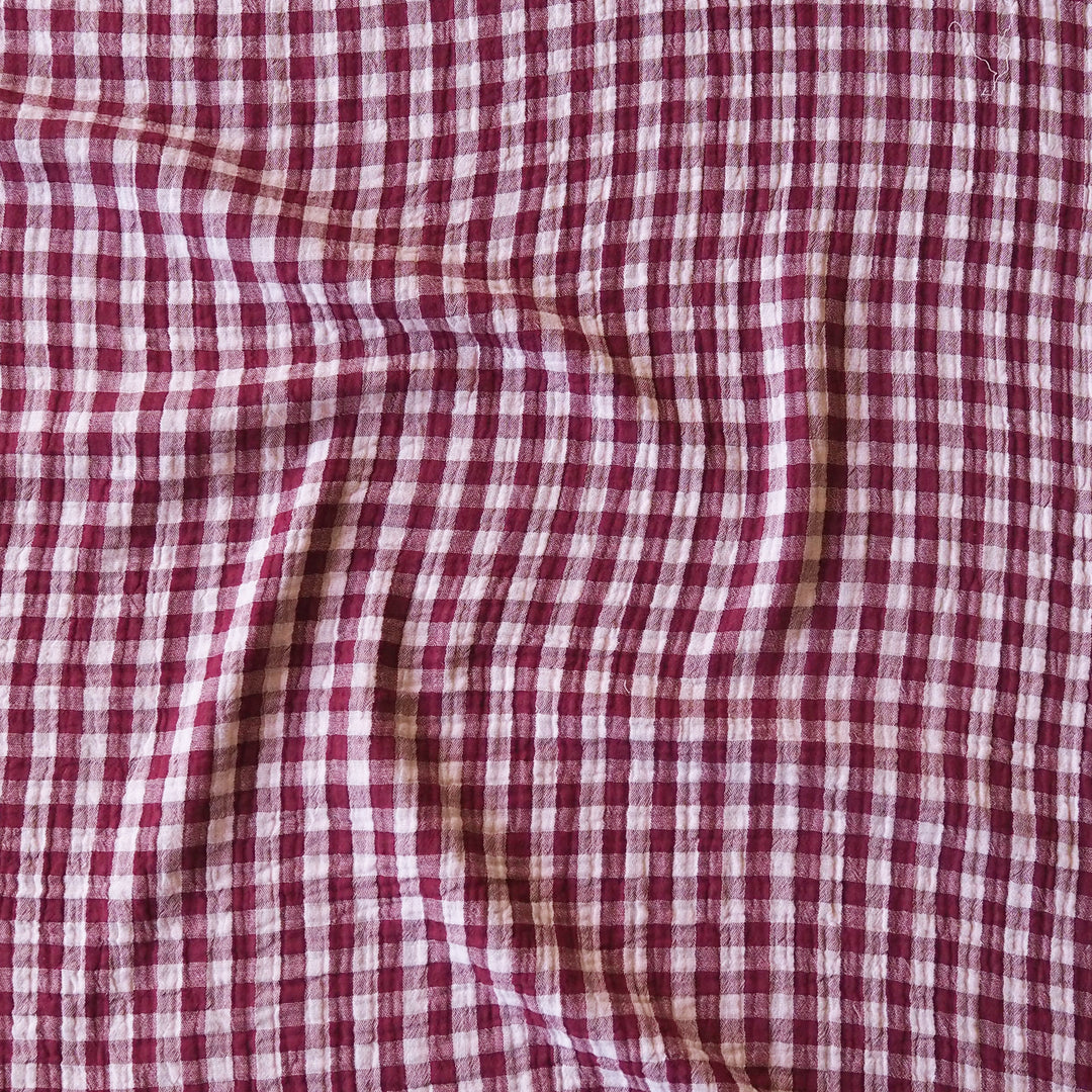 A close-up of a red and white gingham checkered fabric with soft folds and a textured weave.