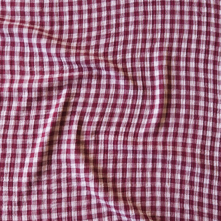 A close-up of a red and white gingham checkered fabric with soft folds and a textured weave.