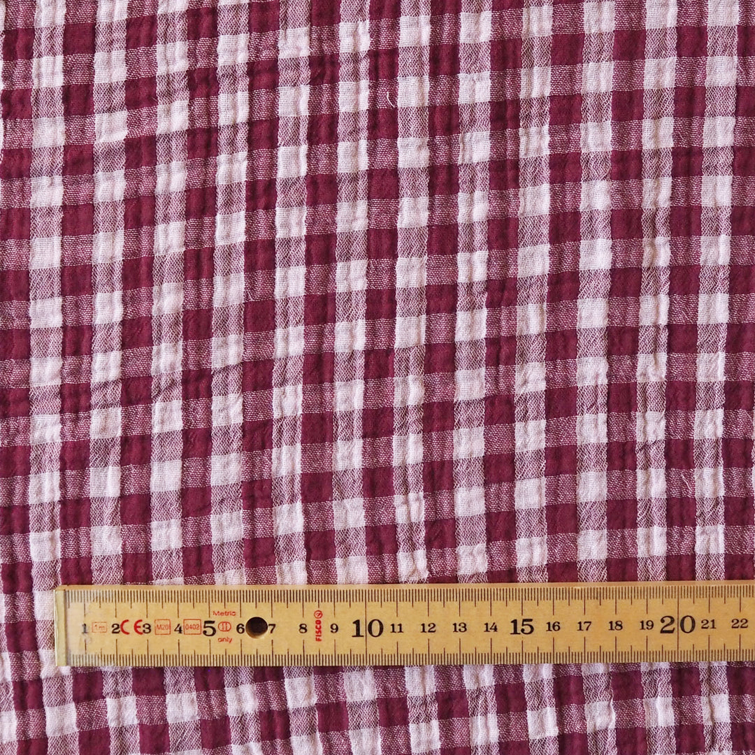 A close-up of a red and white gingham patterned fabric with a wooden ruler at the bottom for scale.