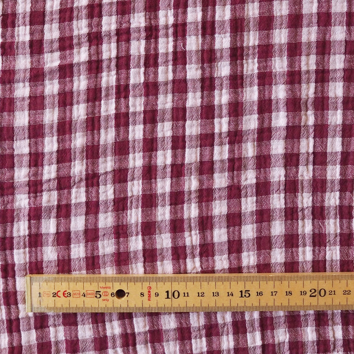 A close-up of a red and white gingham patterned fabric with a wooden ruler at the bottom for scale.