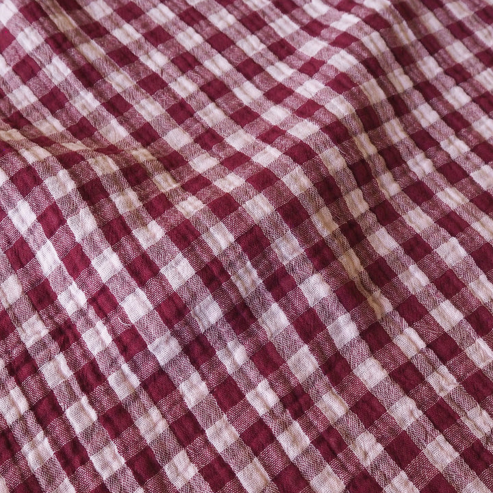 A close-up of a red and white gingham checkered fabric with a soft, crinkled texture.