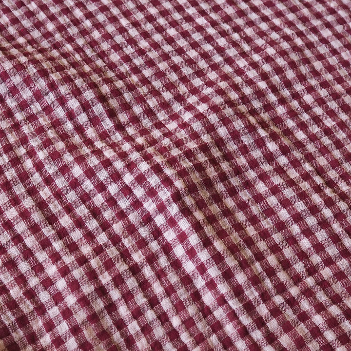 A close-up of a red and white gingham checkered fabric with a textured, slightly wrinkled surface.