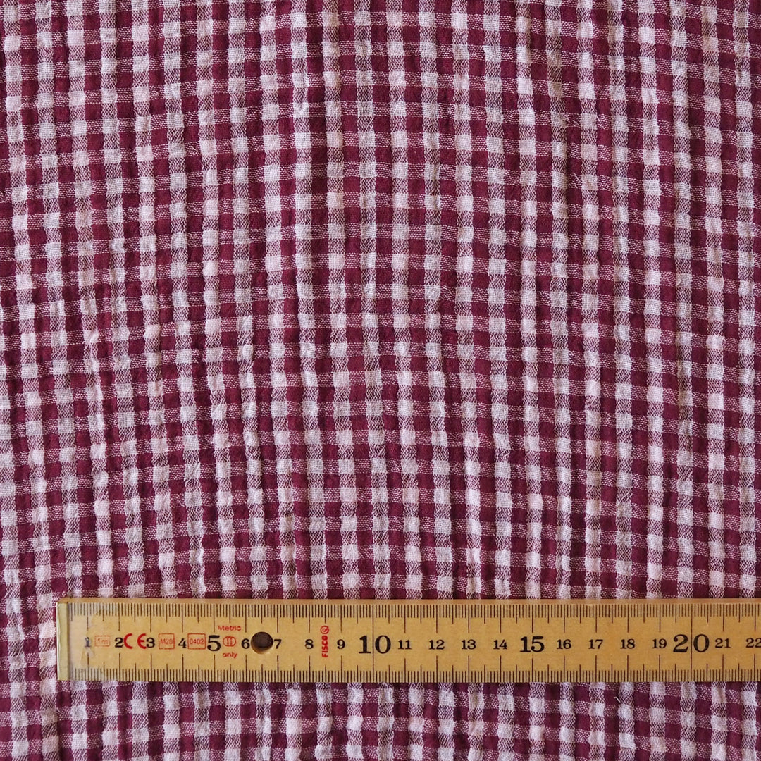 A close-up of a red and white gingham patterned fabric, with a wooden ruler placed along the bottom edge to show scale.