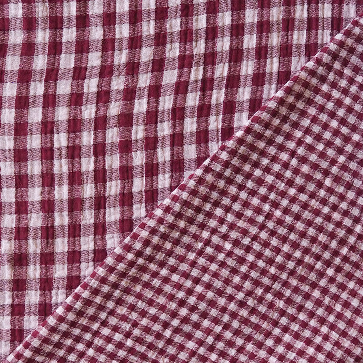 A close-up of a red and white gingham checkered fabric, folded diagonally across the frame.