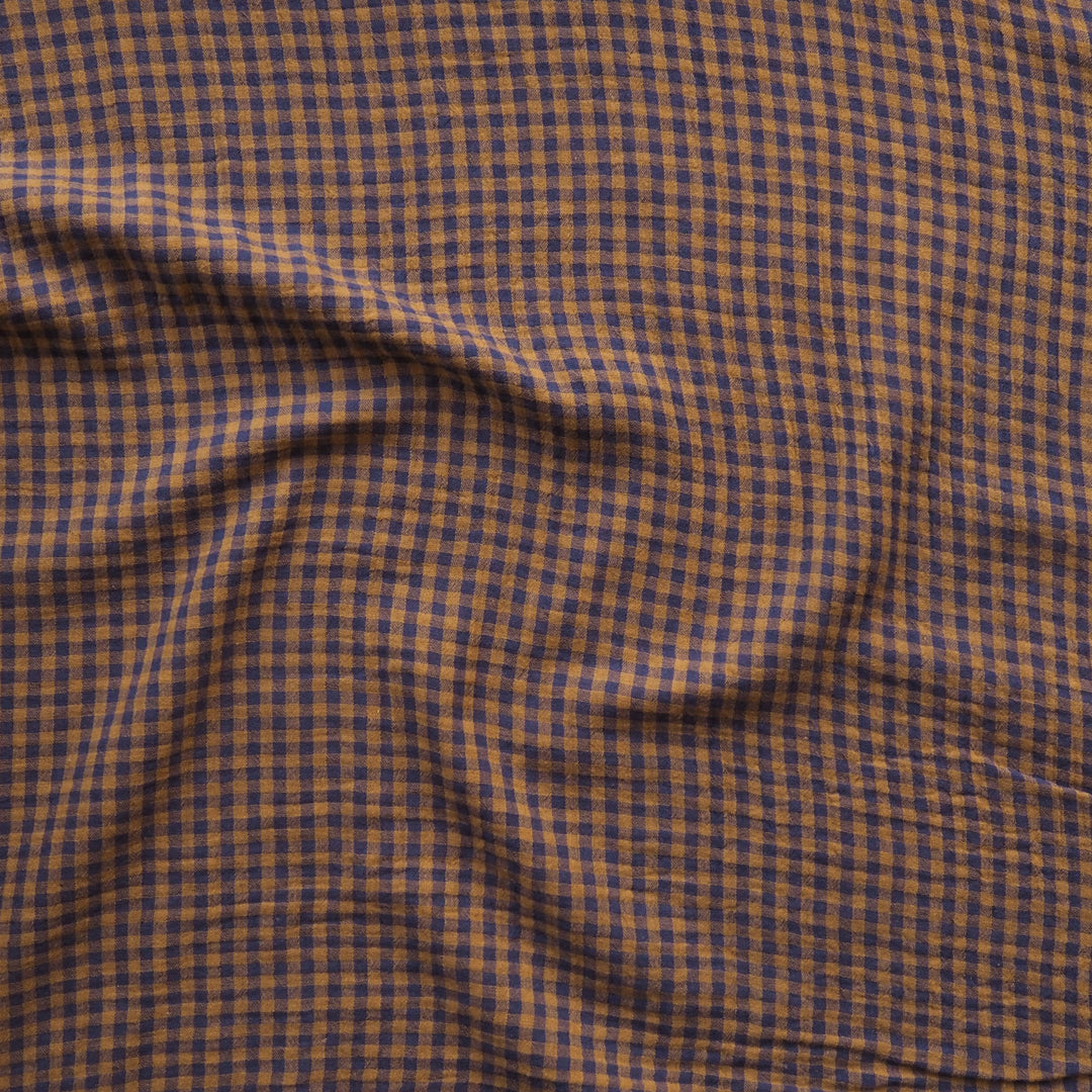 A close-up of a draped fabric with a small-scale brown and dark navy blue gingham check pattern.