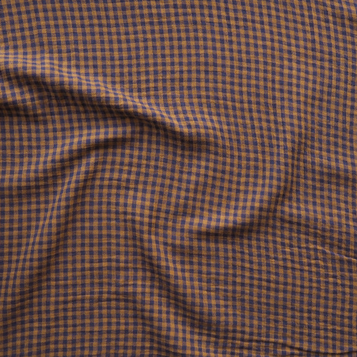 A close-up of a draped fabric with a small-scale brown and dark navy blue gingham check pattern.
