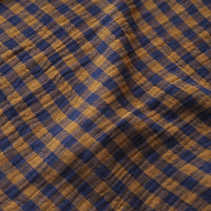 A close-up of a textured fabric with a diagonal gingham plaid pattern in navy blue and mustard yellow.