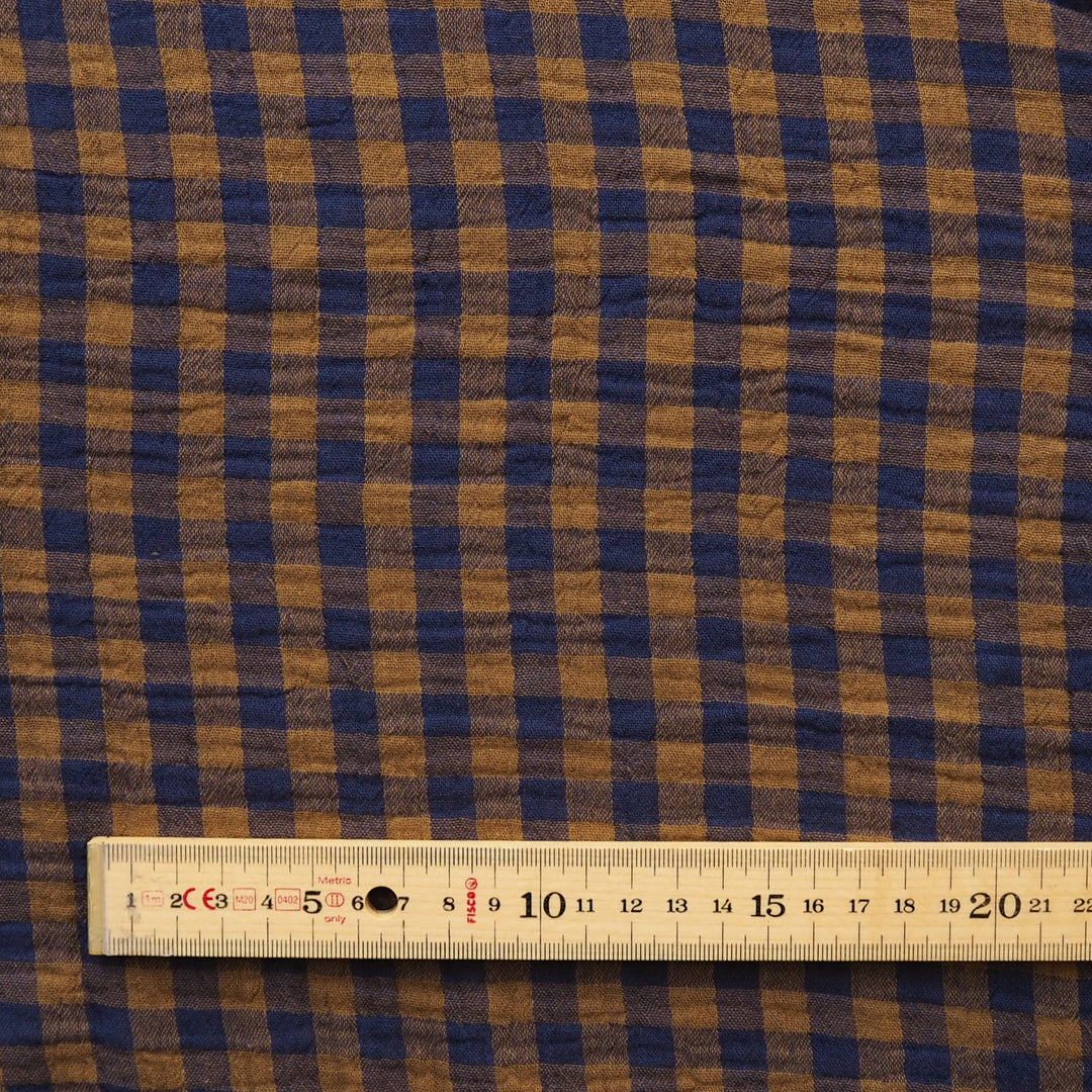A close-up of a brown and navy blue gingham fabric pattern with a wooden ruler at the bottom for scale.