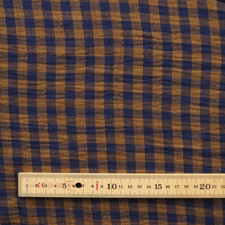 A close-up of a brown and navy blue gingham fabric pattern with a wooden ruler at the bottom for scale.