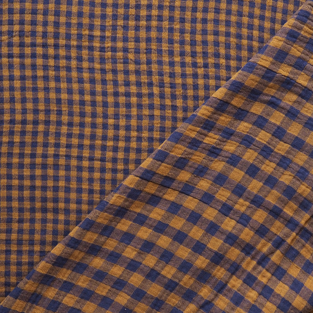A close-up of a checkered fabric with a blue and mustard yellow gingham pattern, folded diagonally across the frame.