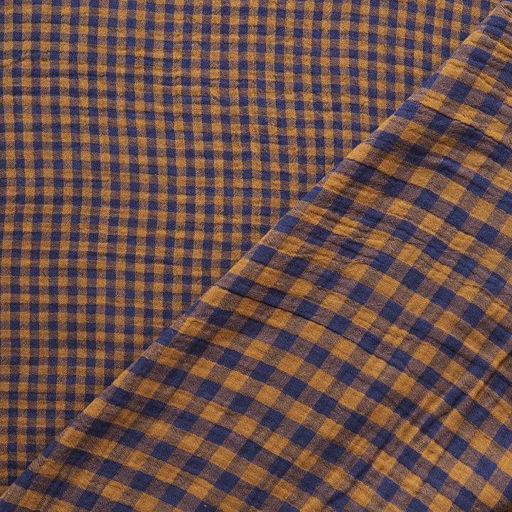 A close-up of a checkered fabric with a blue and mustard yellow gingham pattern, folded diagonally across the frame.