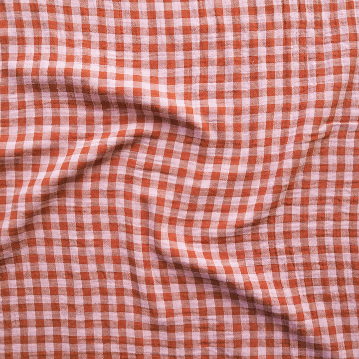 A close-up of a red and white gingham checkered fabric with soft folds and a textured linen-like weave.