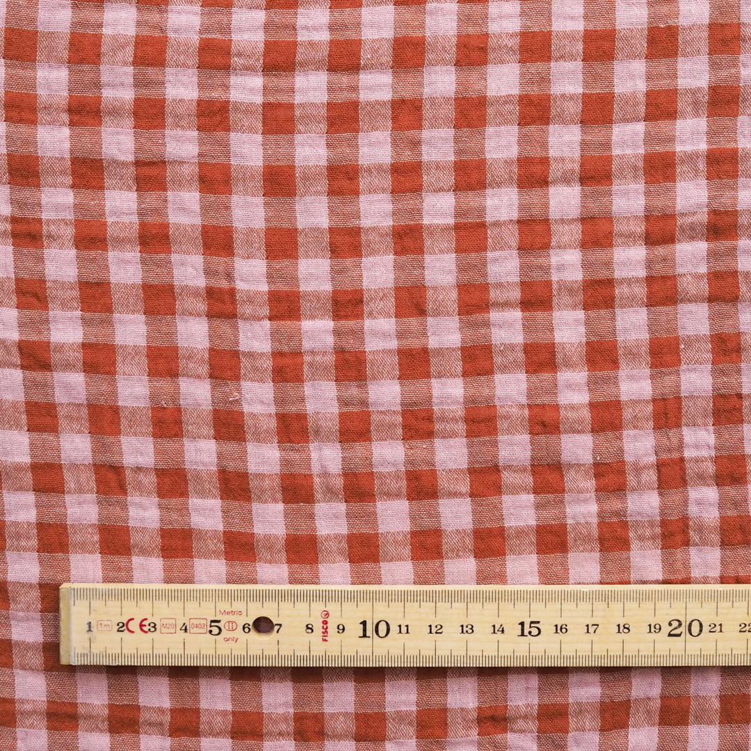 A close-up of red and white gingham fabric with a wooden ruler at the bottom for scale.