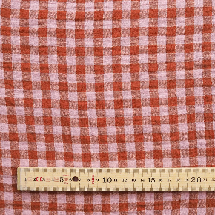 A close-up of red and white gingham fabric with a wooden ruler at the bottom for scale.