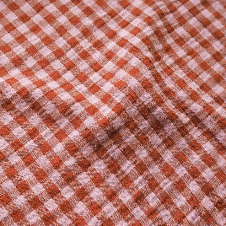 A close-up of a red and white gingham checkered fabric with a soft, draped texture.