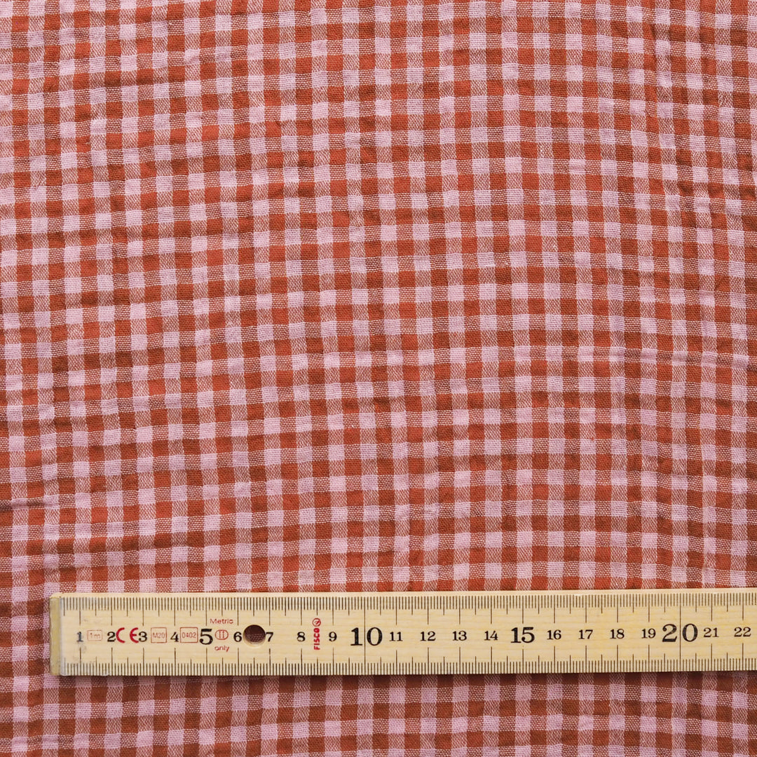 A close-up of a red and white gingham fabric pattern with a wooden ruler at the bottom for scale.