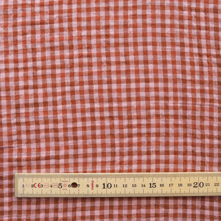 A close-up of a red and white gingham fabric pattern with a wooden ruler at the bottom for scale.
