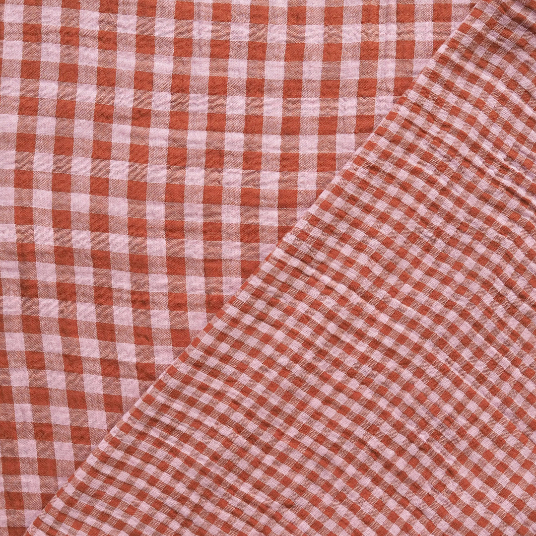 A close-up of a red and white gingham checkered fabric, folded diagonally across the frame.