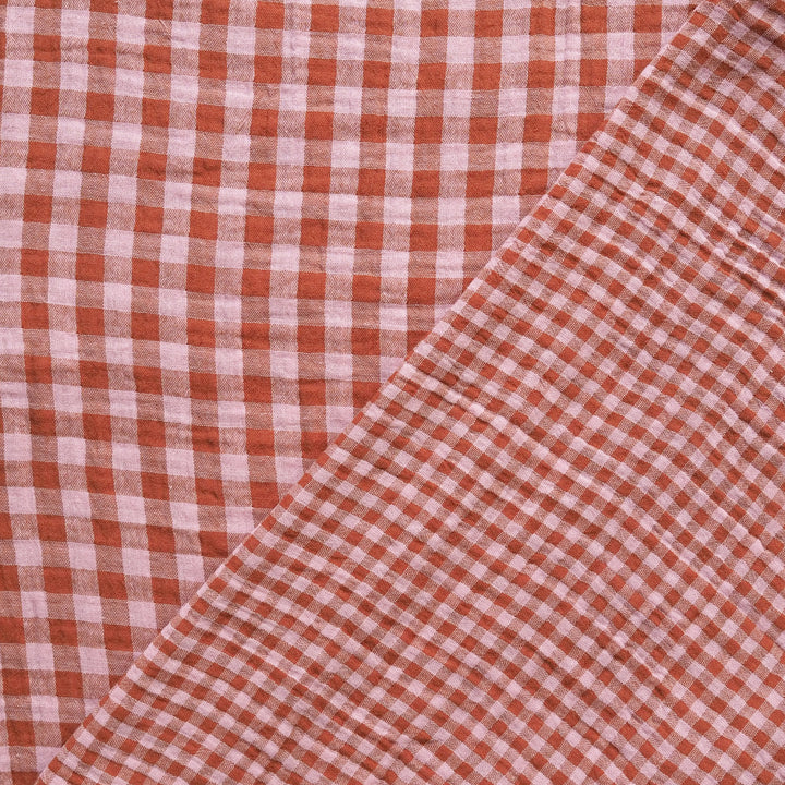 A close-up of a red and white gingham checkered fabric, folded diagonally across the frame.