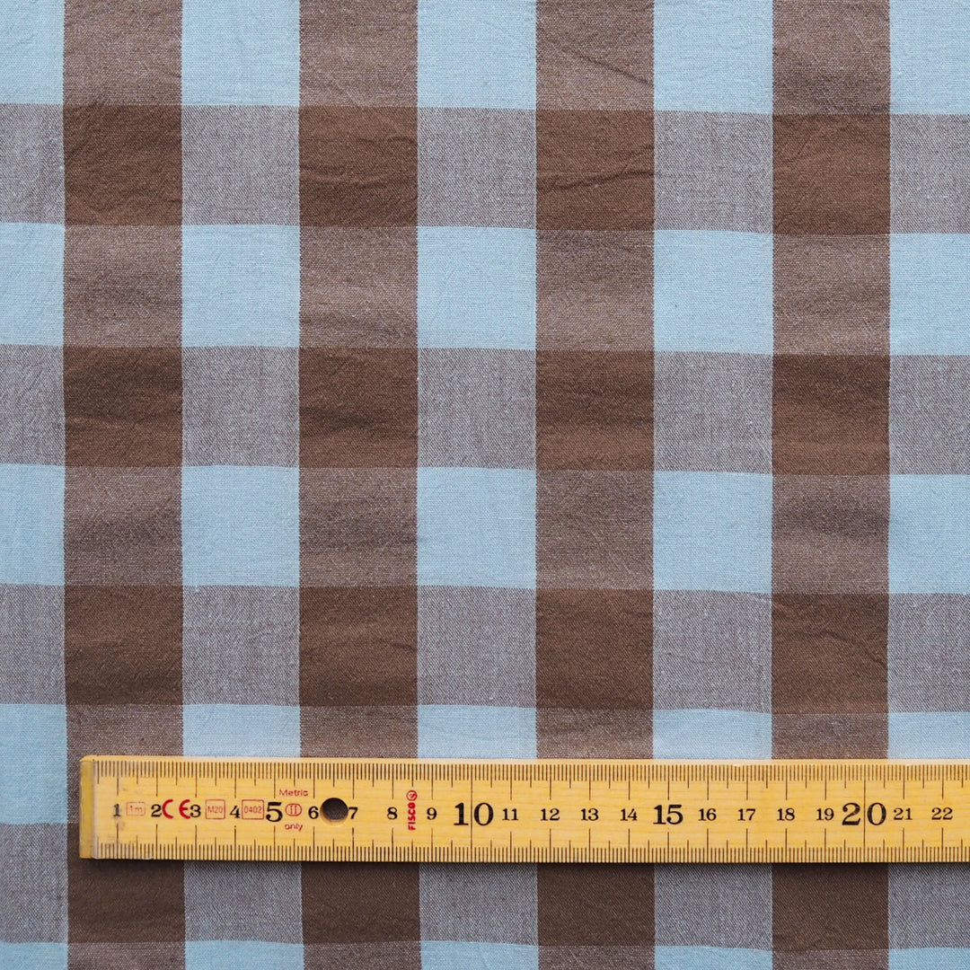 Brown and light blue gingham fabric with a wooden ruler at the bottom for scale.