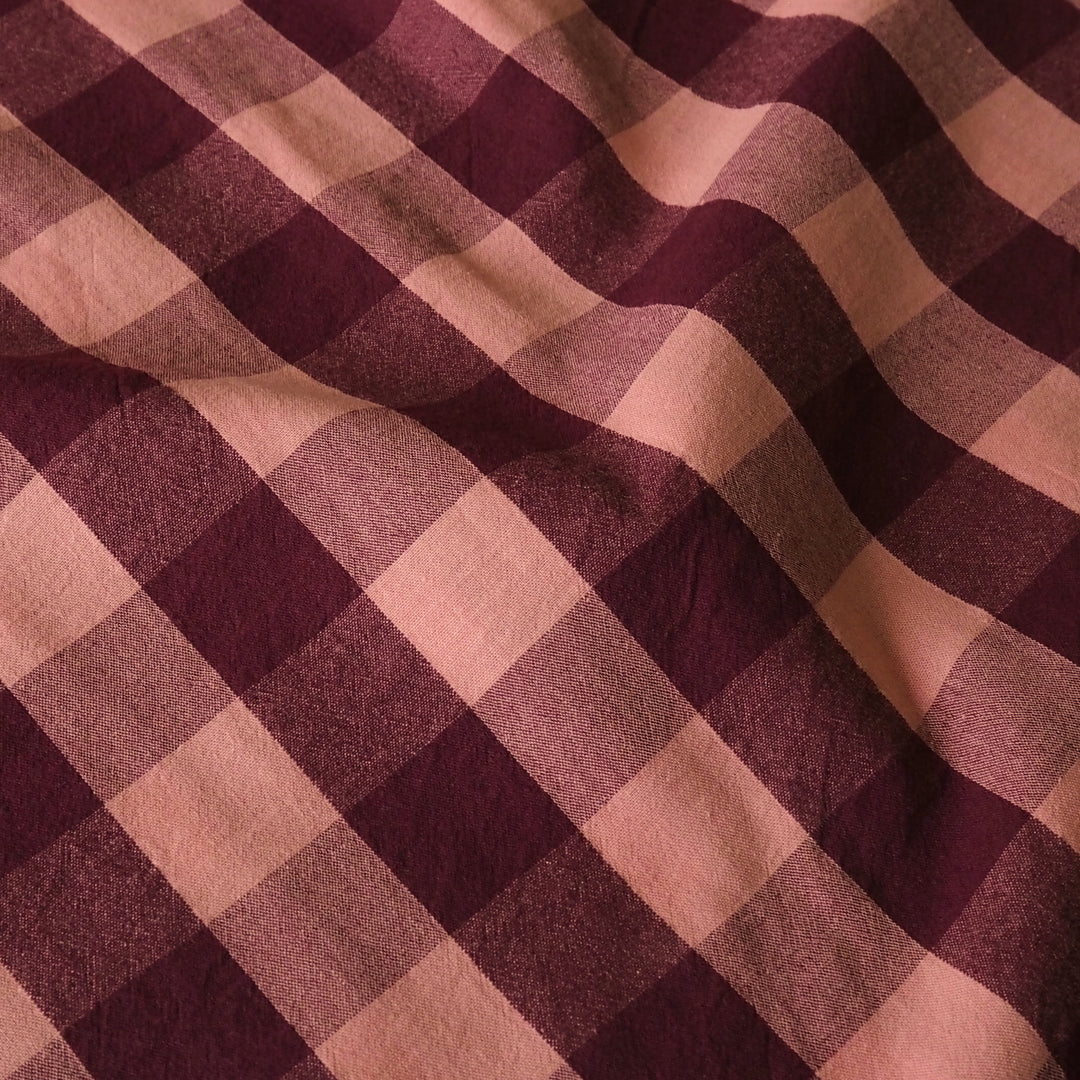 A close-up of a plaid fabric with alternating diagonal stripes in deep burgundy and dusty rose pink, showing a soft woven texture.