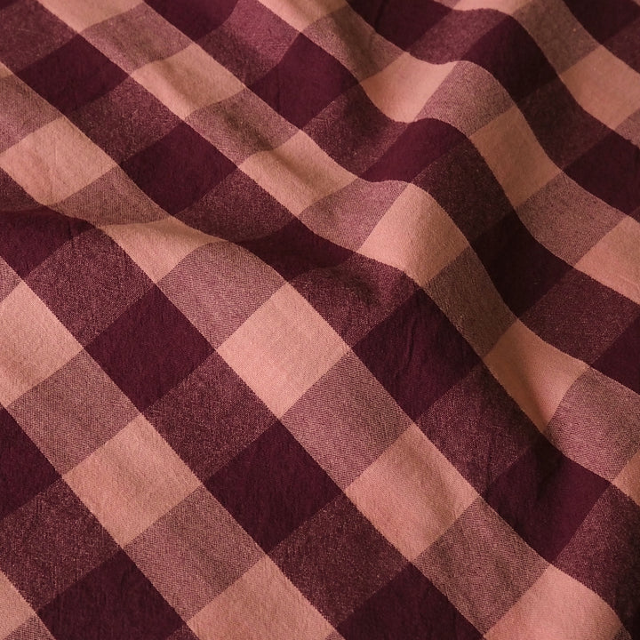 A close-up of a plaid fabric with alternating diagonal stripes in deep burgundy and dusty rose pink, showing a soft woven texture.