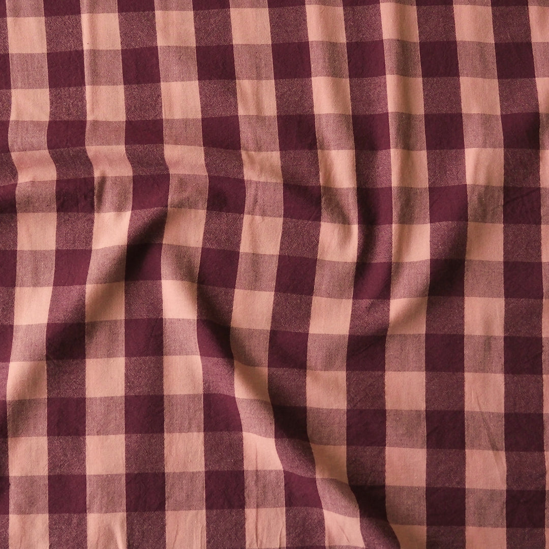 A close-up of a draped fabric with a classic gingham check pattern in deep burgundy and dusty pink.