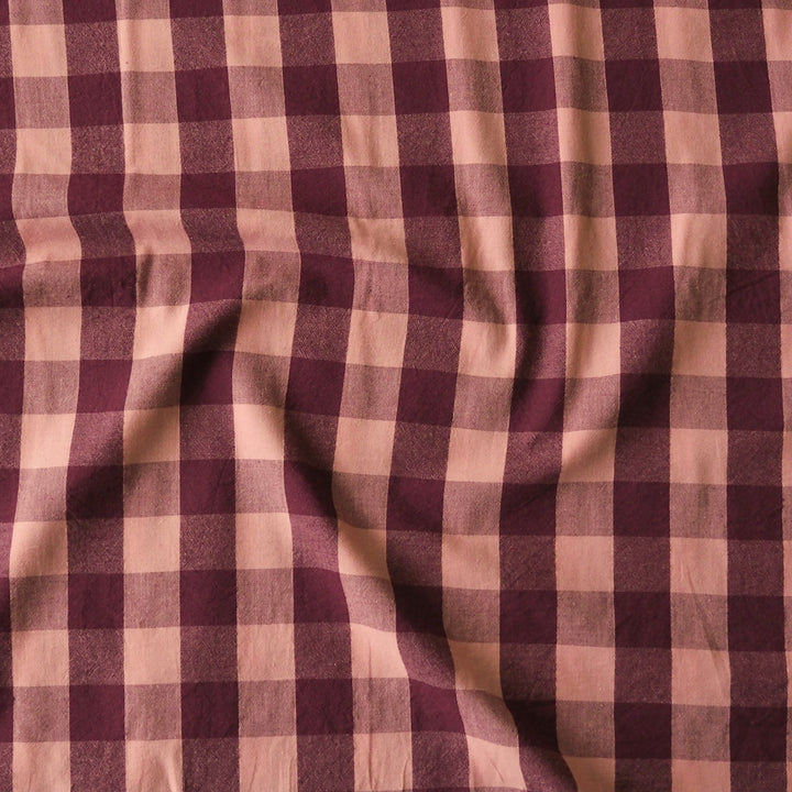 A close-up of a draped fabric with a classic gingham check pattern in deep burgundy and dusty pink.