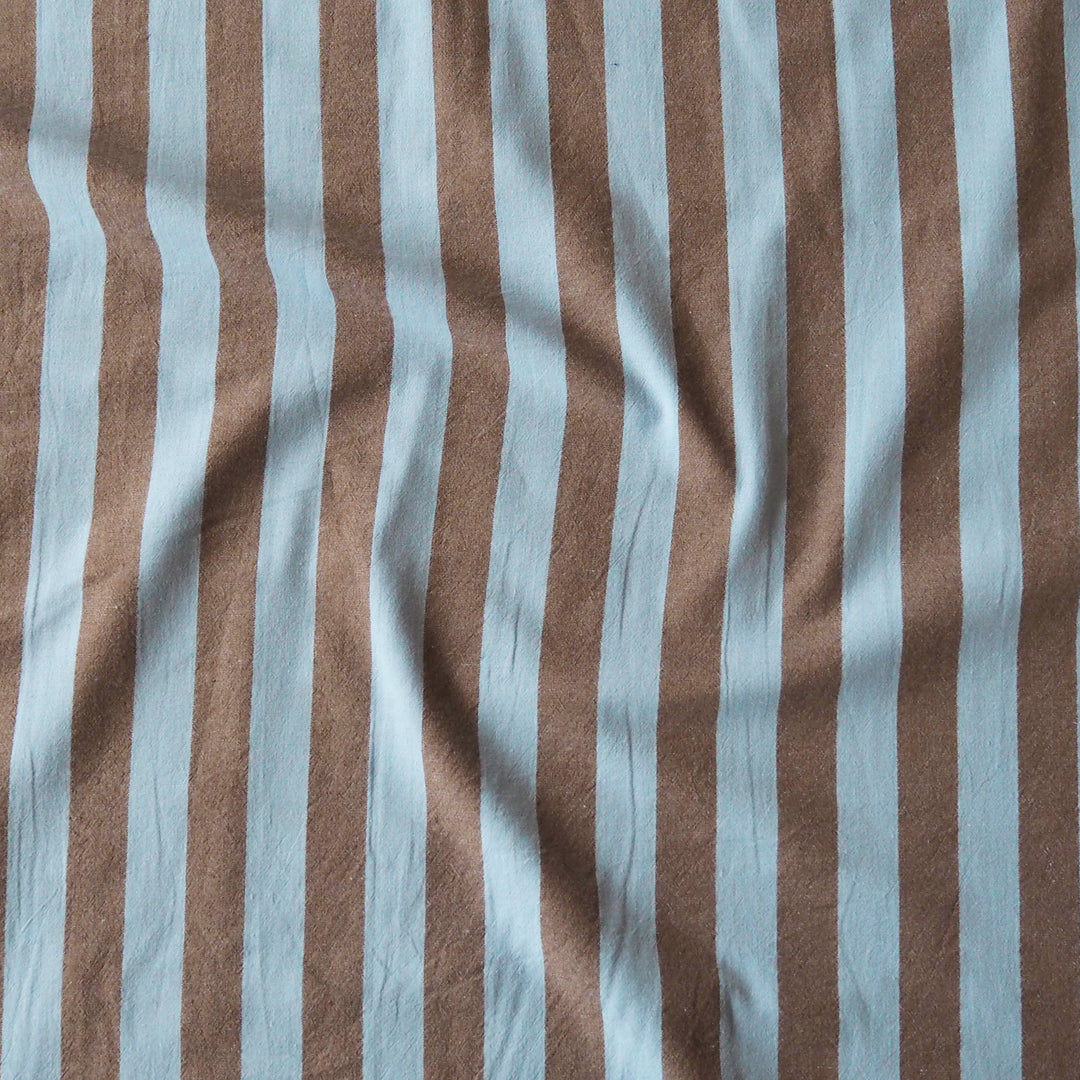 A close-up of vertically striped fabric with alternating light blue and warm brown stripes, shown with soft folds and texture.