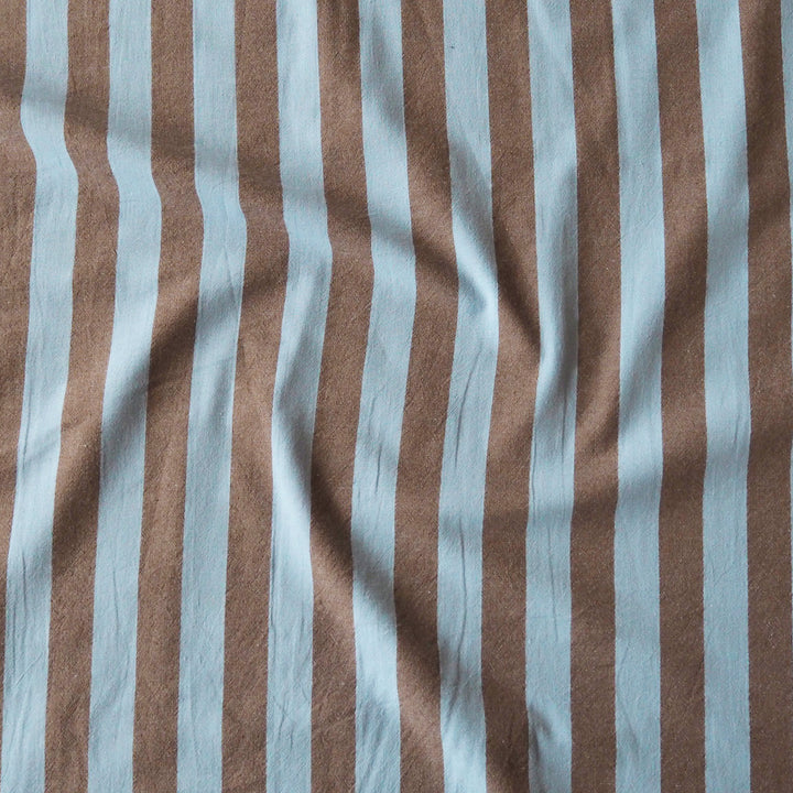 A close-up of vertically striped fabric with alternating light blue and warm brown stripes, shown with soft folds and texture.